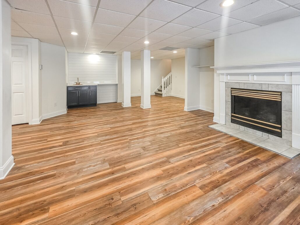 Basement fireplace with a painted mantel, with the wet bar and stairs beyond, at 1030 Billy Mantle Lane