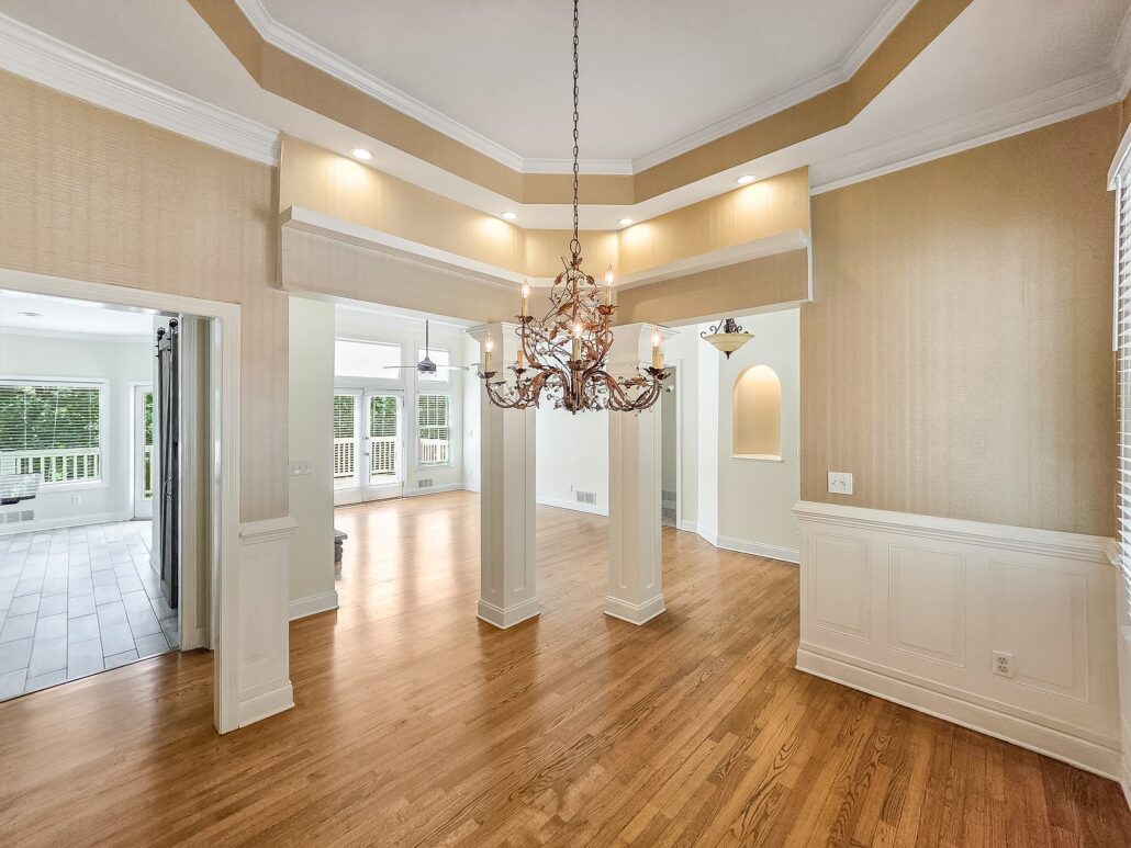 Dining room with a tray ceiling, chandelier and wainscoting, open to the living room through square columns, at 1030 Billy Mantle Lane