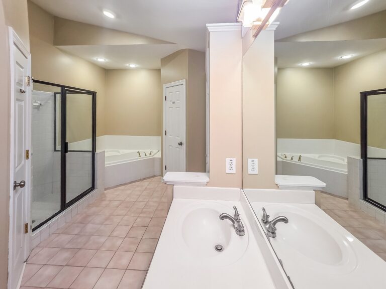 Primary bathroom vanity with a glass-enclosed shower and corner tub beyond at 1030 Billy Mantle Lane