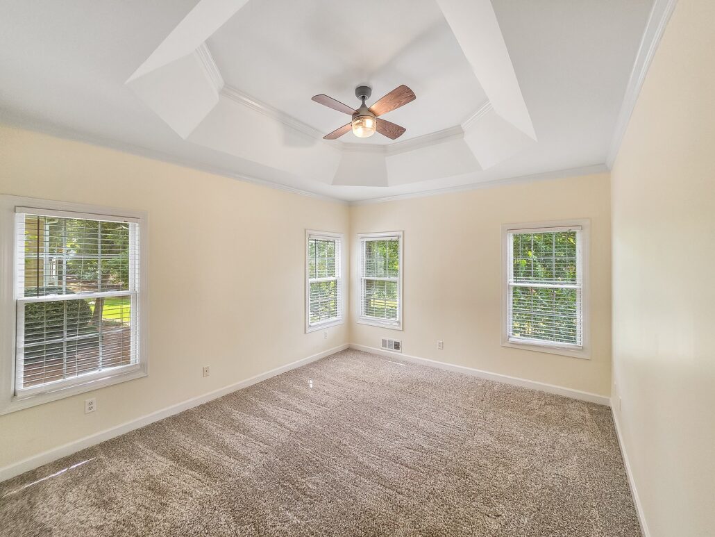 Main-level primary bedroom with a tray ceiling and windows on three walls at 1030 Billy Mantle Lane