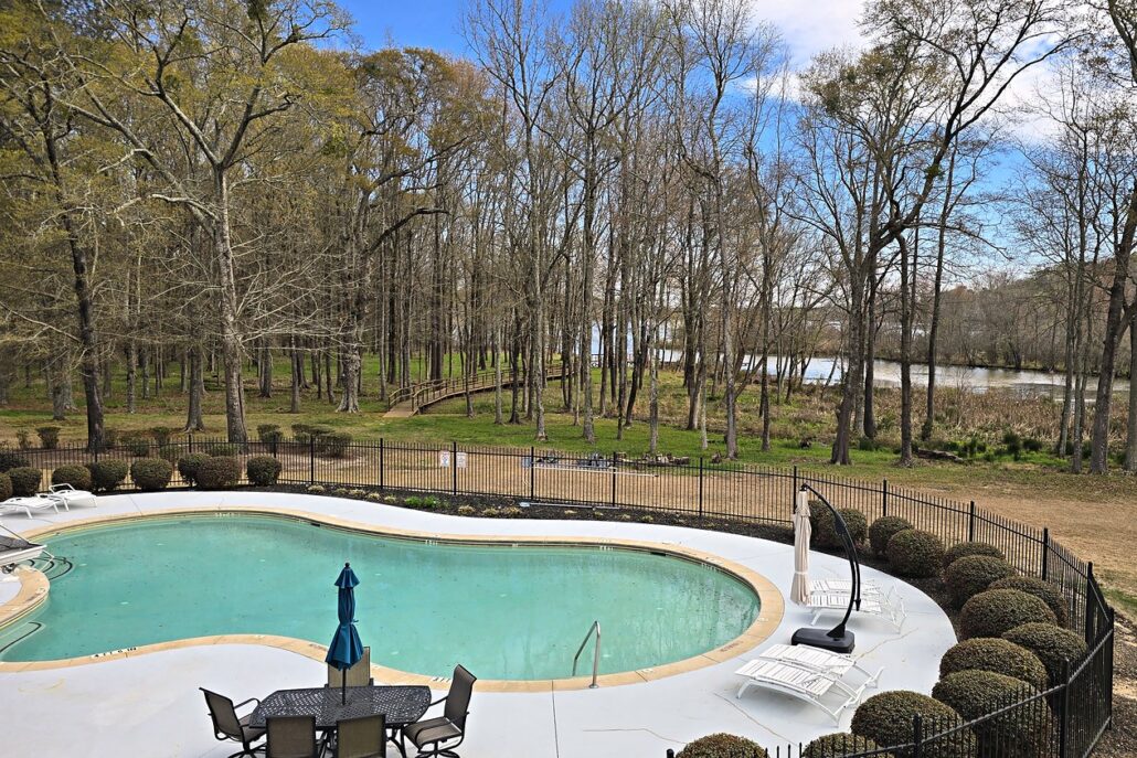 Fenced community pool with the lake beyond the trees, behind an end-unit townhome at Lake Oconee