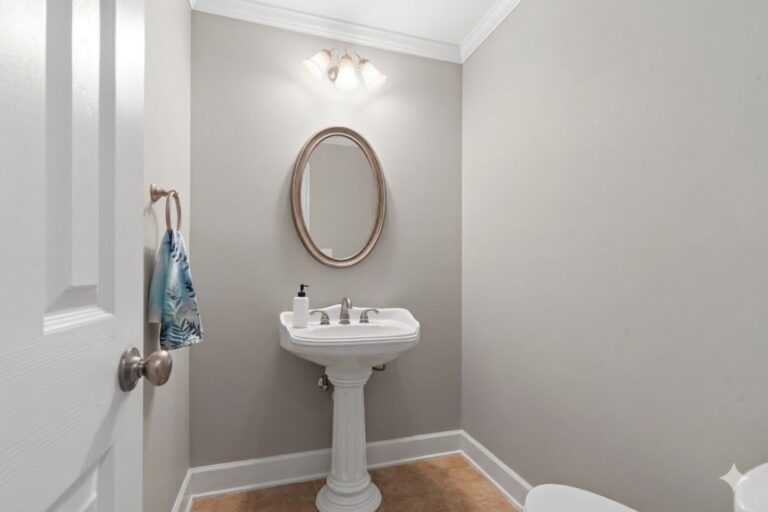 Main-level half bath with a pedestal sink and oval mirror in a Carriage Cove townhome on Lake Oconee
